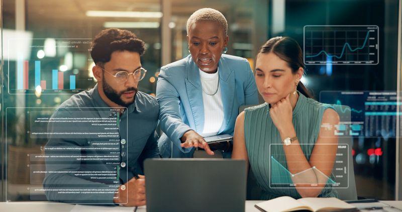 Business people, night and coaching with laptop, hud or hologram for market analysis at office. Group, employees or discussion with computer data or digital overlay for online statistics at workplace