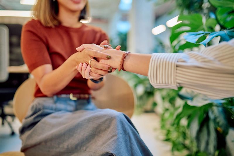 Close-up of hands holding each other during psychological support session in modern office with plants
