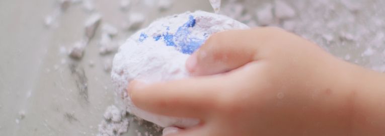 Child's hand handling white powdery substance with blue paint.