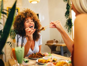 Two women enjoying a meal together with chopsticks.