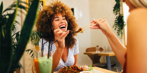Two women enjoying a meal together, sharing food with chopsticks.