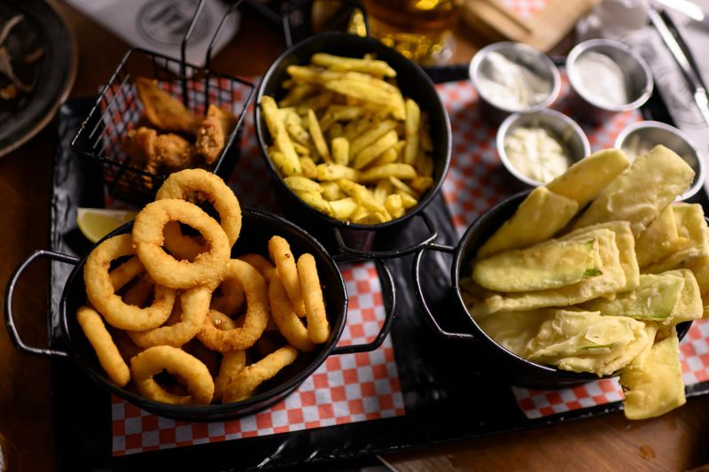 Close up shot of dishes with onion rings, chicken wings, potatoes, deep dish on a table in a pub. Outdoor eating, nightlife, restaurants, socialising.