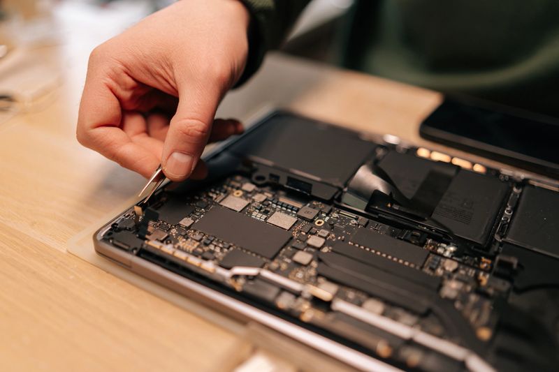 Close-up of skilled technician using tweezers assembling component on laptop motherboard, performing maintenance and troubleshooting in repair workshop. Concept of process electronic device repair.