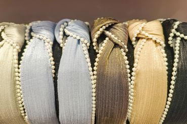A row of six fabric headbands with pearl accents in various colors.