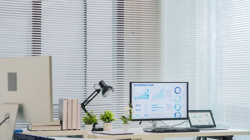 A clean and organized office desk featuring a computer screen displaying business analytics and charts, surrounded by potted plants, folders, and a desk lamp, representing a professional and productive work environment.