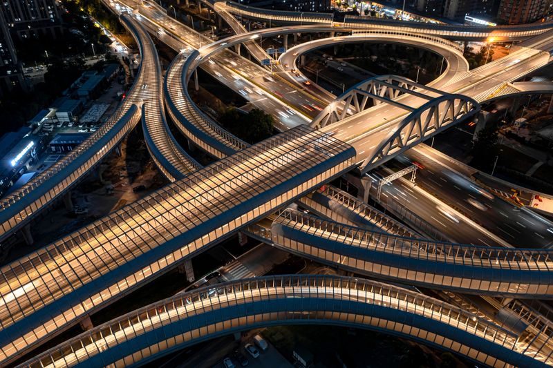Aerial view of a complex highway interchange at night, with illuminated roads and bridges in an urban setting, showcasing modern infrastructure.