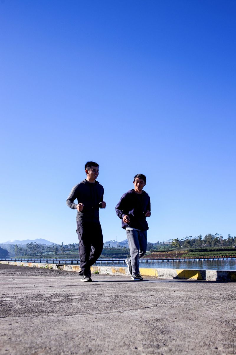 Two Young Men Jogging Along a Lakeside Path With Mountain Views