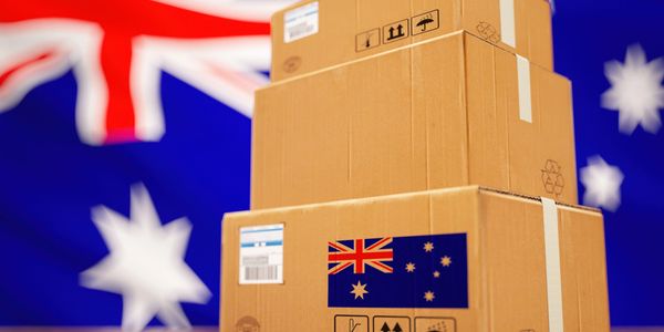 Stacked cardboard boxes with Australian flag labels on wooden floor.