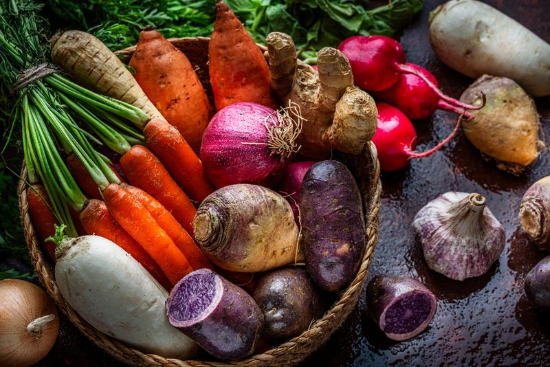 Fresh organic root vegetables shot from above on kitchen table. Healthy eating or vegetarian food in a wicker basket.