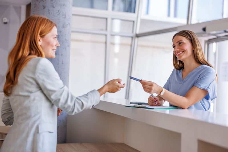 Smiling receptionist receiving medical insurance card from a patient in a modern clinic