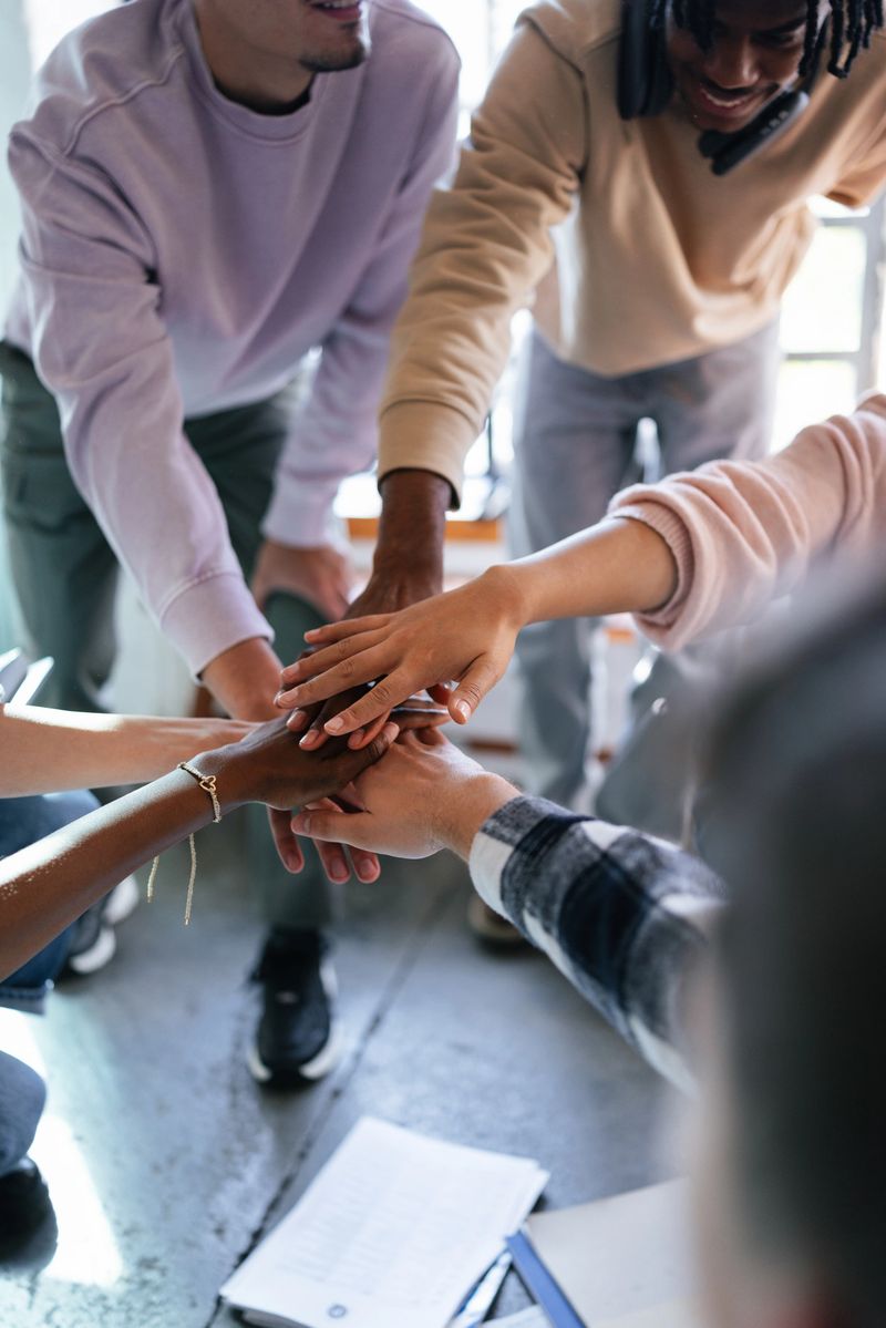 An energetic group of students coming together with hands stacked, symbolizing unity, friendship, and cooperation within an educational environment. Capturing the essence of teamwork and collaboration in a modern learning space.