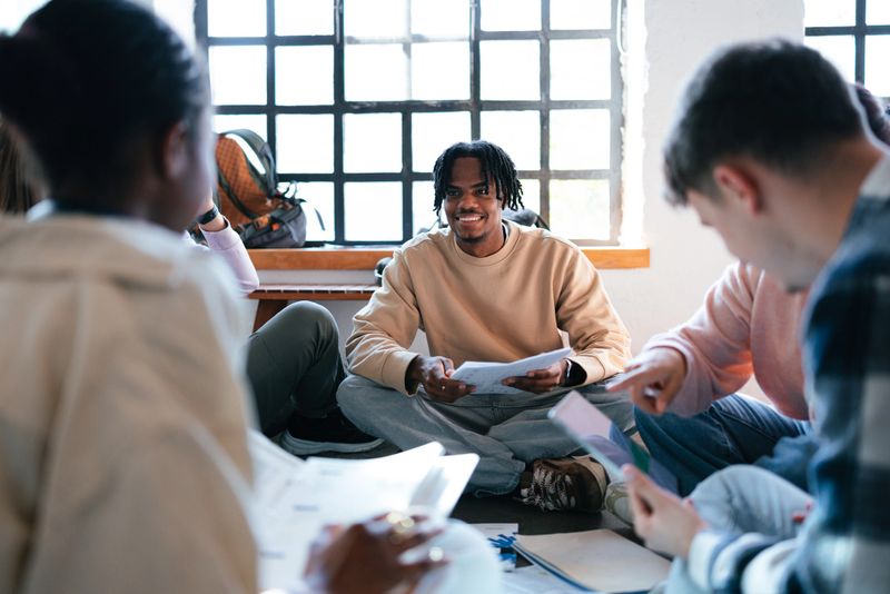 A group of diverse students seated in a circle, joyfully collaborating on educational materials in a well-lit classroom, fostering teamwork, learning, and enthusiastic engagement.