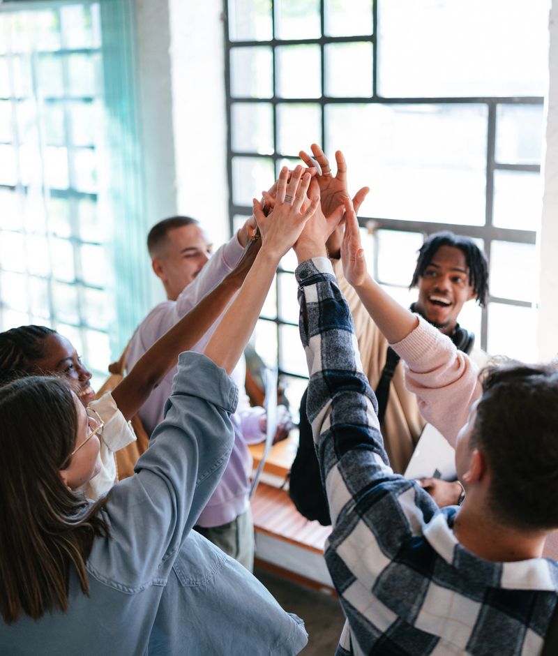 Young friends celebrating with a team high-five. They show unity, positivity, and teamwork in a cheerful and modern setting.