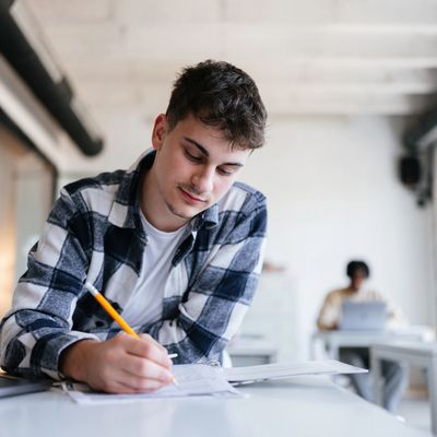 Young man focused on writing in a bright classroom.