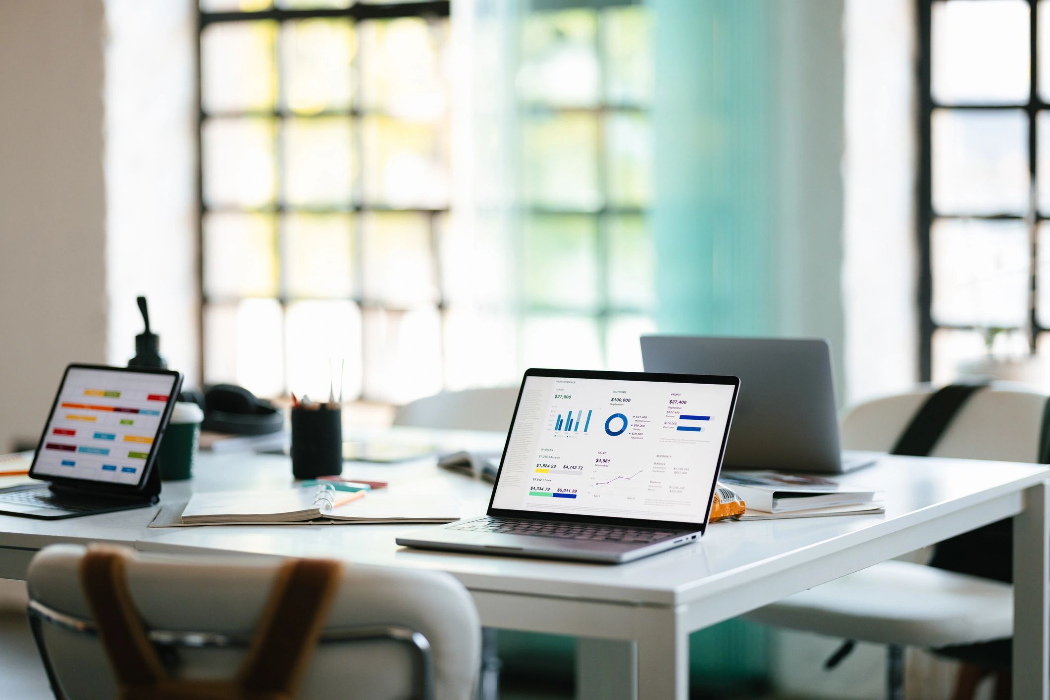 Modern office workspace with laptops displaying charts and data on a white table.