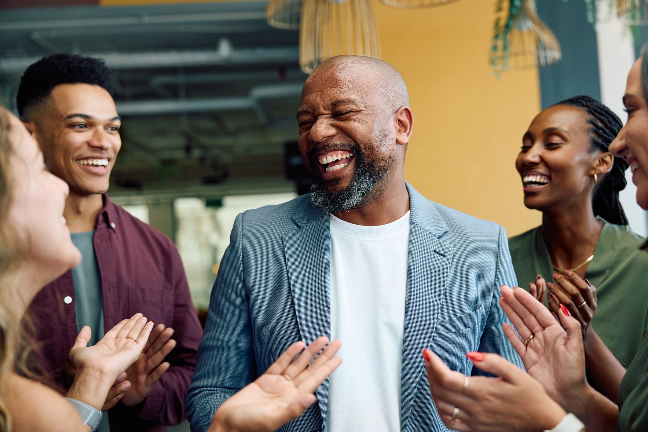 A man laughs joyfully surrounded by clapping friends.