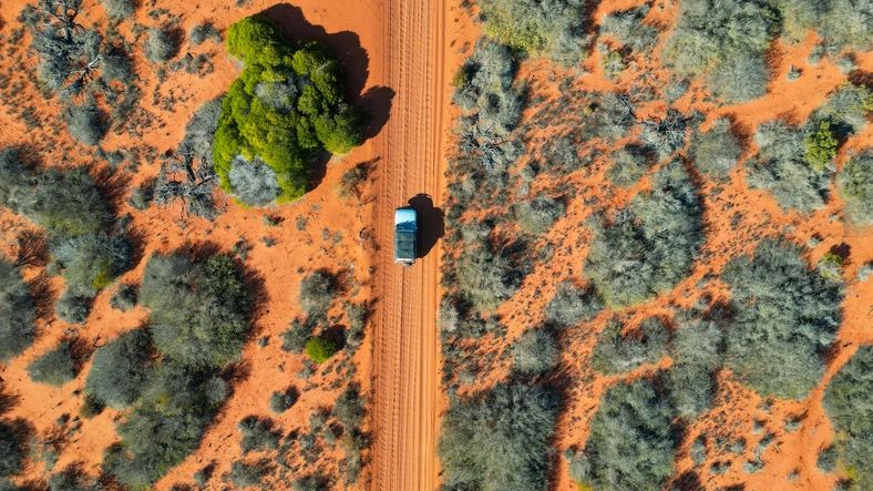 A car driving through the red soil of Australia, photograped with a drone