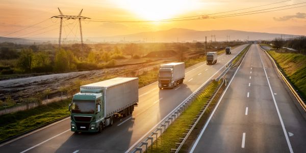 Several trucks driving on a highway during sunset.