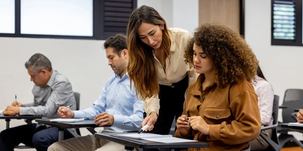 A woman helps a student in a classroom setting.