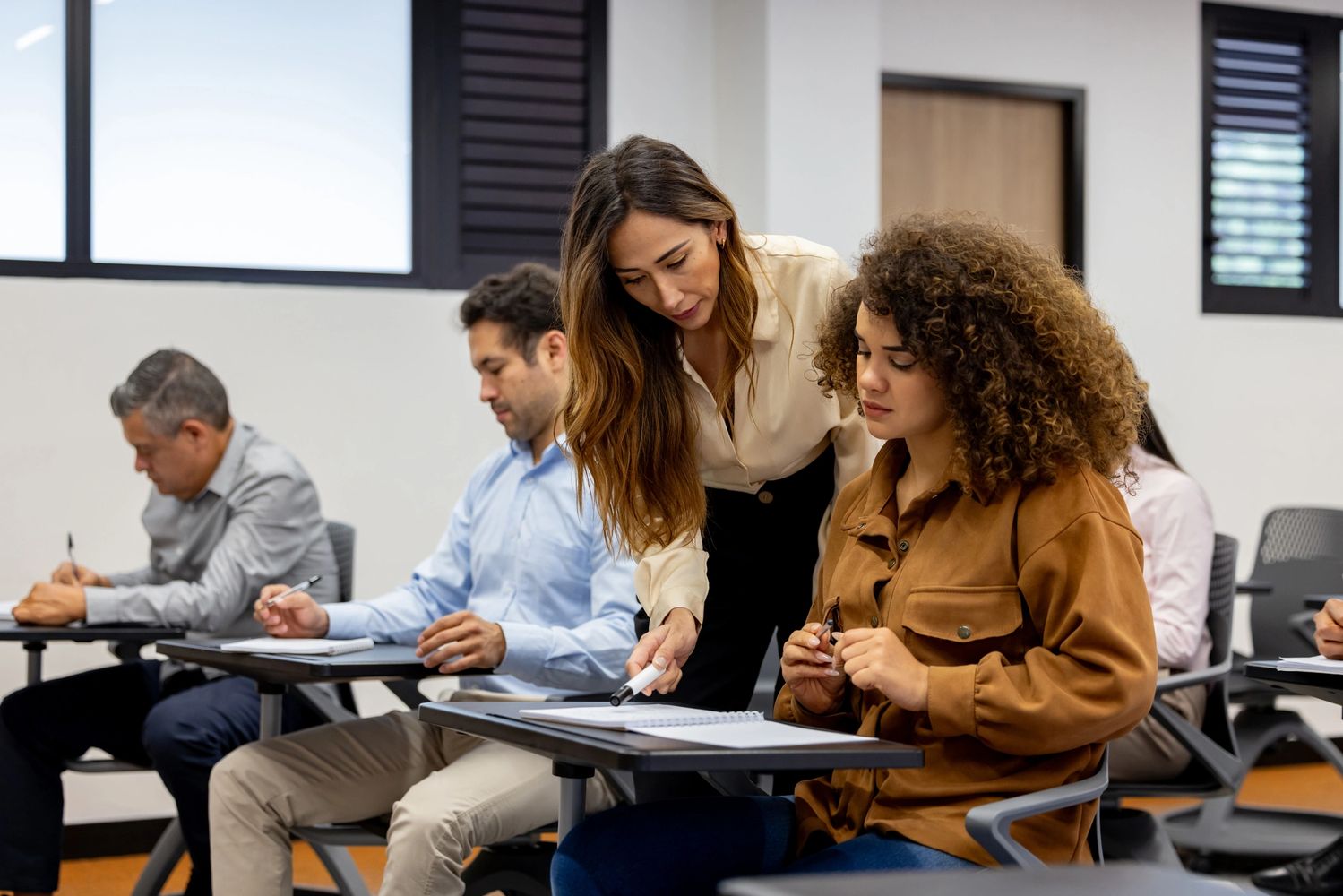 A woman helps a student in a classroom setting.