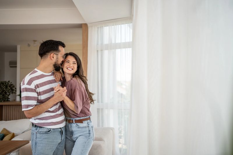 Young couple dancing and smiling together in their cozy living room, savoring a romantic moment filled with love and joy, creating lasting memories in their comfortable home