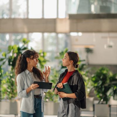 Two professionals in conversation in a bright modern building, one holding a tablet and the other a 