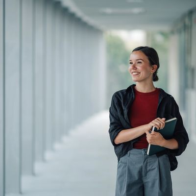 Young woman smiling with a book in a hallway.