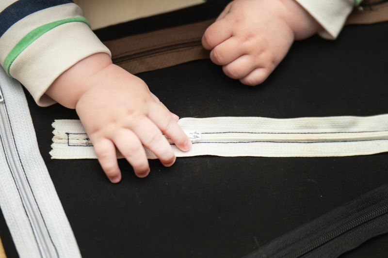 Child's hands practicing fine motor skills by attempting to unzip a fastener on a homemade learning board.