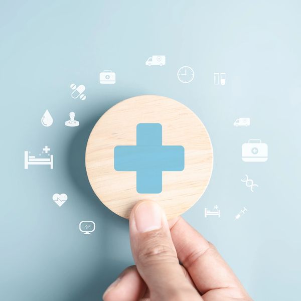 Hand holding wooden disc with blue medical cross and floating icons.