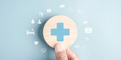 Hand holding a wooden circle with a blue medical cross and healthcare icons around it.