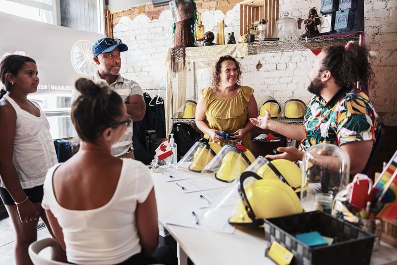 Multiracial family with two teenage children visiting rage room. LGBTQ+ Business owner is greeting them. All dressed in summer casual clothes. Interior of Rage Room gym in downtown Hamilton, Ontario in Canada.