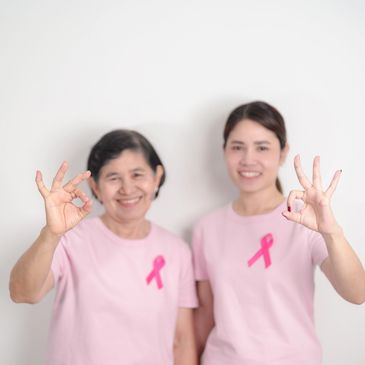 Two women in pink shirts with pink ribbons showing OK signs.