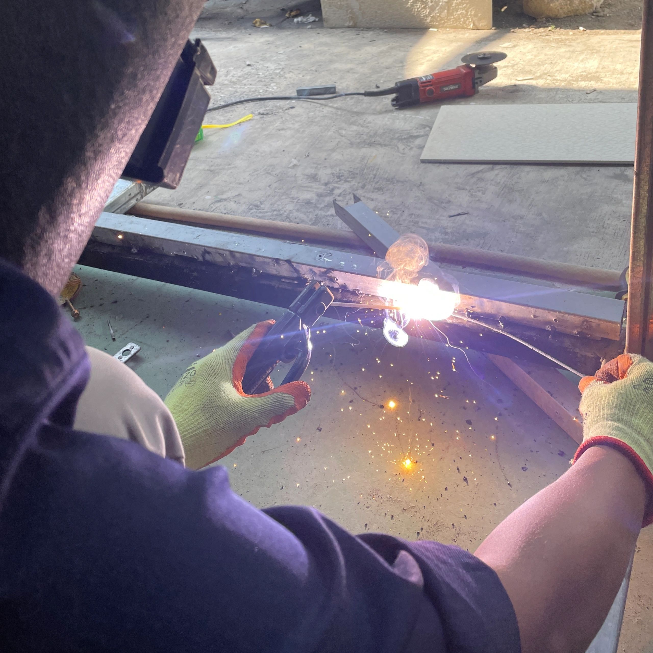 Person welding metal with sparks flying, wearing protective gloves and mask.