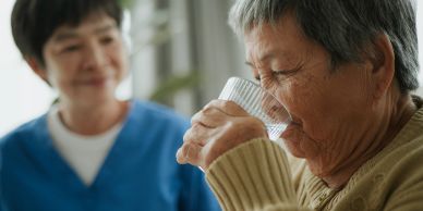 Oudere man drinkt water, vrouw kijkt toe.