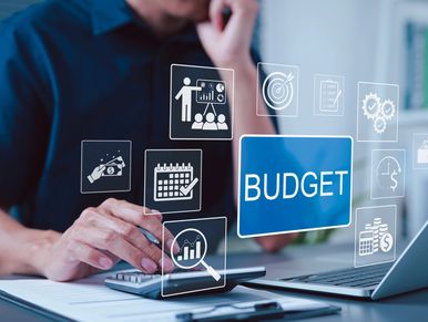 Person calculating budget with financial icons and laptop.