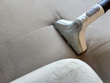 A vacuum cleaner deep cleaning a beige fabric surface.