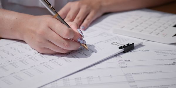Person marking financial figures on printed documents with a pen.