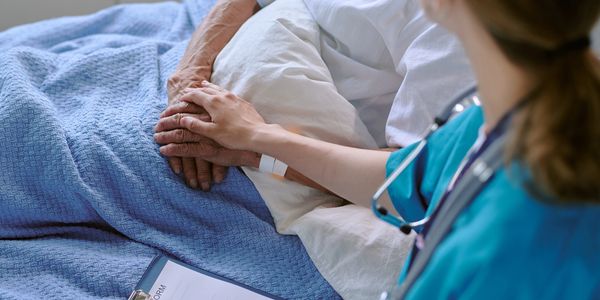 Nurse holding patient's hand in hospital bed.