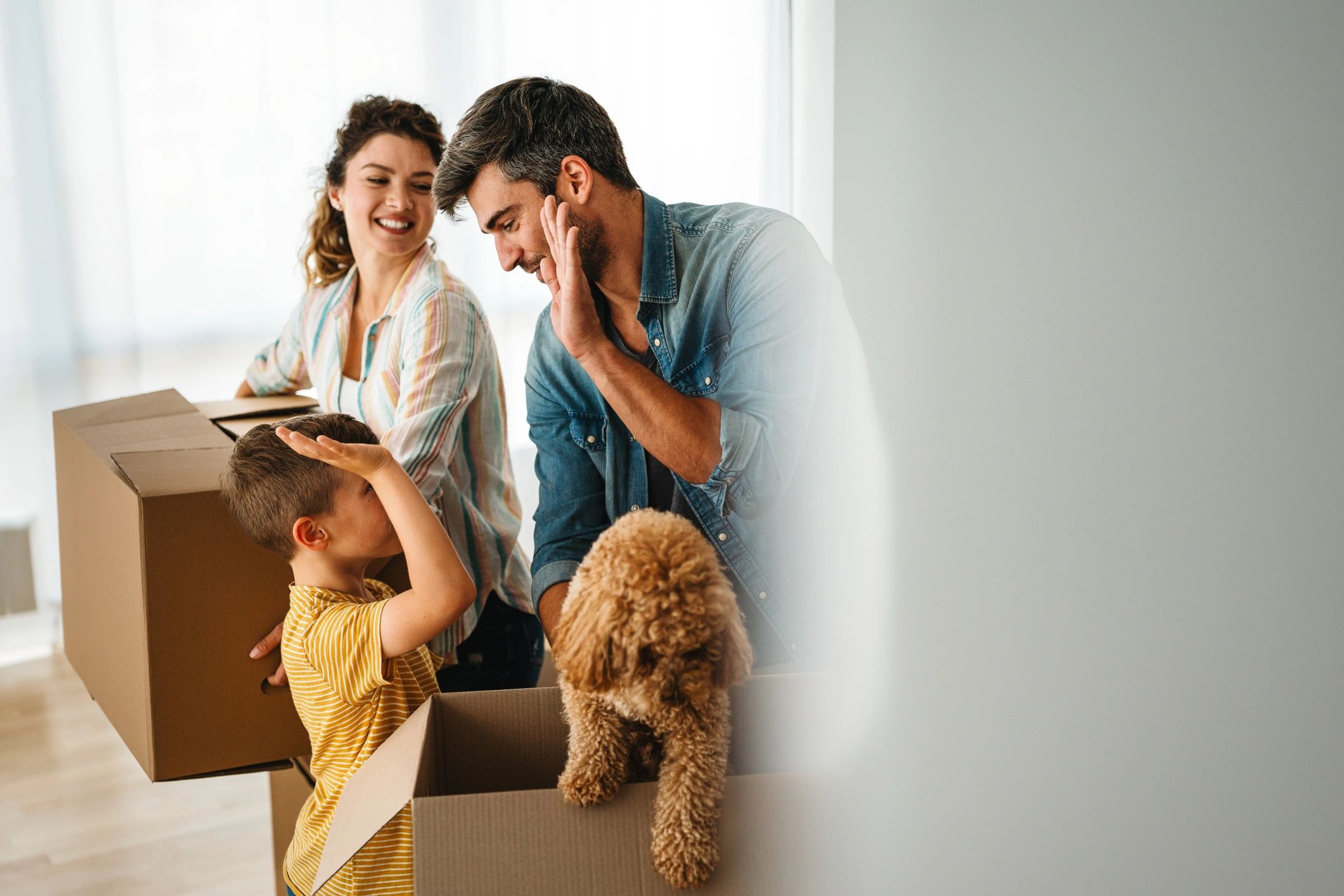 A happy family of three moving into a new home with their small dog, who is playfully sitting inside