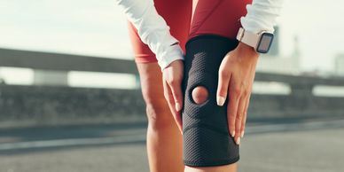 Person holding knee with brace outdoors.