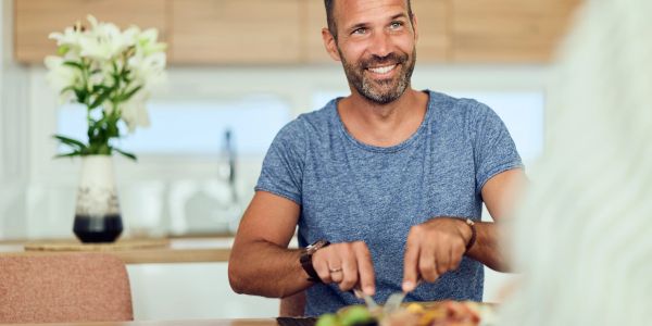 Smiling man enjoys a meal at home, cutting food on his plate.