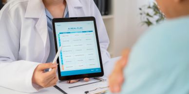 Doctor mostrando un plan de comidas en una tableta a un paciente.