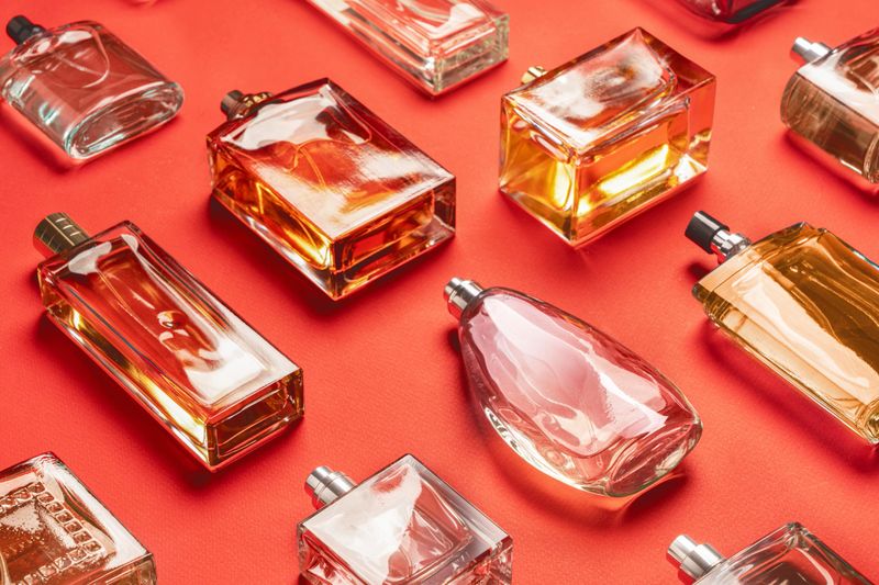 A captivating display showcases various elegant perfume bottles arranged on a striking red background. Each bottle reflects light beautifully, highlighting its unique design and color. The diverse shapes and sizes reveal the artistry behind fragrance creation, while their glossy surfaces enhance the luxurious appeal. This collection invites viewers to appreciate the beauty of cosmetics and the aromatic experiences they offer.