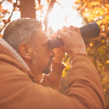 Man with gray hair uses binoculars outdoors in autumn.