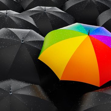 Bright rainbow umbrella stands out among black umbrellas in rain.
