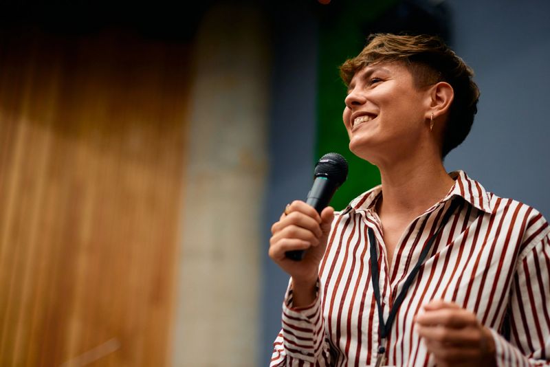 Smiling female entrepreneur engaging an audience while delivering an inspiring presentation at a business conference held in a bustling convention center
