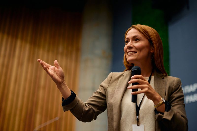 Businesswoman confidently gesturing while speaking into a microphone. Engaging the audience during a corporate conference. Sharing expertise and inspiring growth through her motivational presentation