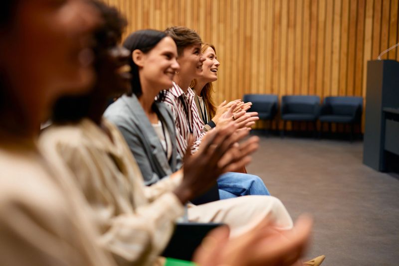 Group of businesspeople sitting together in a row, enthusiastically applauding the speaker following an inspiring and successful business conference meeting, filled with positive energy