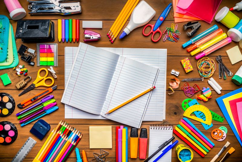 Back to school themes. Top view of stationery on wood desk with paper notepad and frame of school office supplies