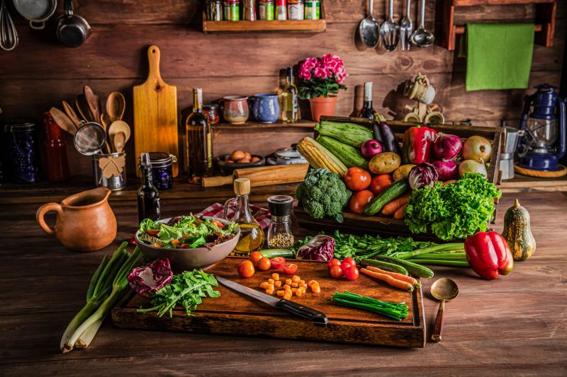 Fruit and vegetable themes: Making a vegan salad in rustic kitchen with assorted organic vegetables: Bell Red Peppers, carrots, lettuce, olive oil, peppermint, potatoes, onions, celery, broccoli, carrots, cucumber, Zucchini, rugula, eggplant, corn